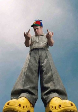 Low-angle shot of a man in a propeller beanie towering into the sky, wearing enormous yellow Crocs