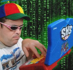 A man in a propeller beanie and pink sunglasses typing on a children's toy laptop in front of falling green Matrix code