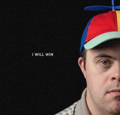A stern close-up portrait of a man in a pastel propeller beanie in low light, captioned: I WILL WIN
