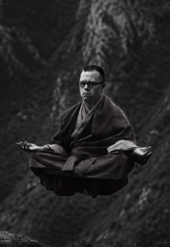 Black and white photograph of a man in monk robes levitating cross-legged above a mountain ridge