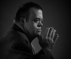 Black and white portrait of a man in profile, hands pressed together in prayer, eyes closed